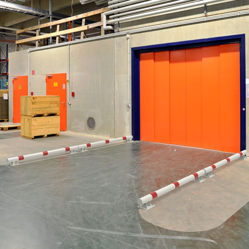 Erhöhte, weiß-rote Rammschutzbalken als Anfahrschutz vor einer großen Industrietür in einer Lagerhalle.